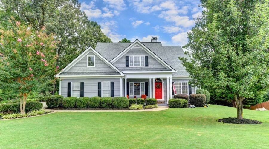 Gray craftsman-style home with a red front door and a manicured front lawn